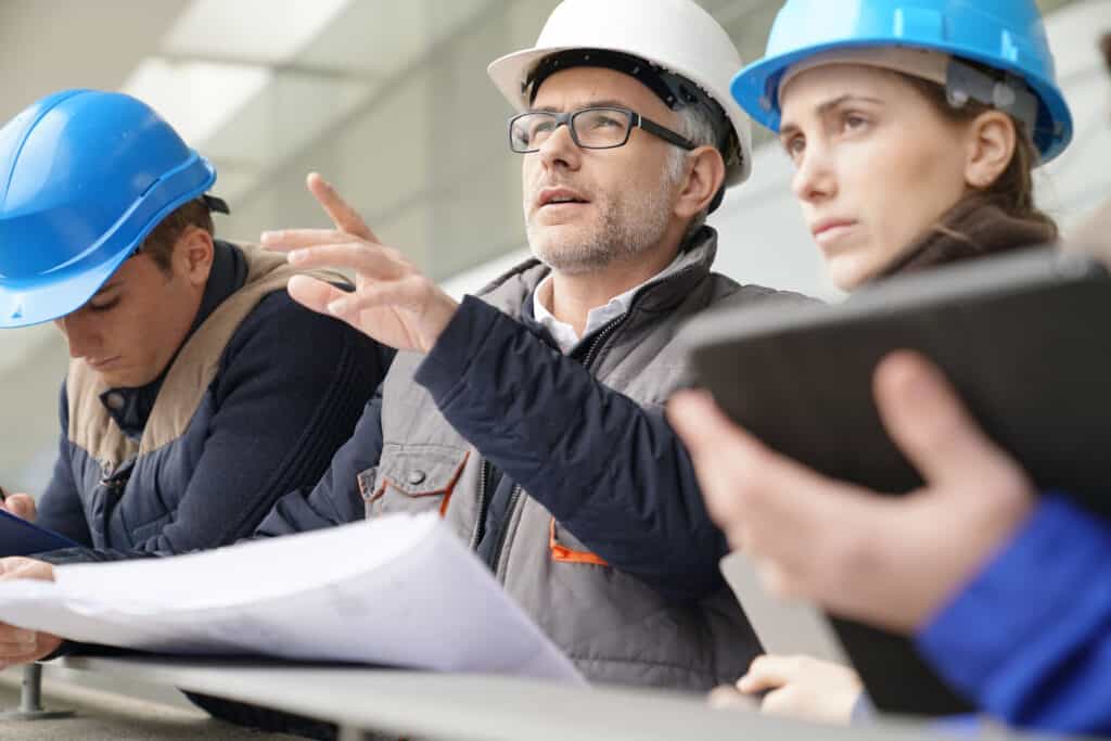 High-angle of construction professionals in safety helmets discussing project plans outside construction site.