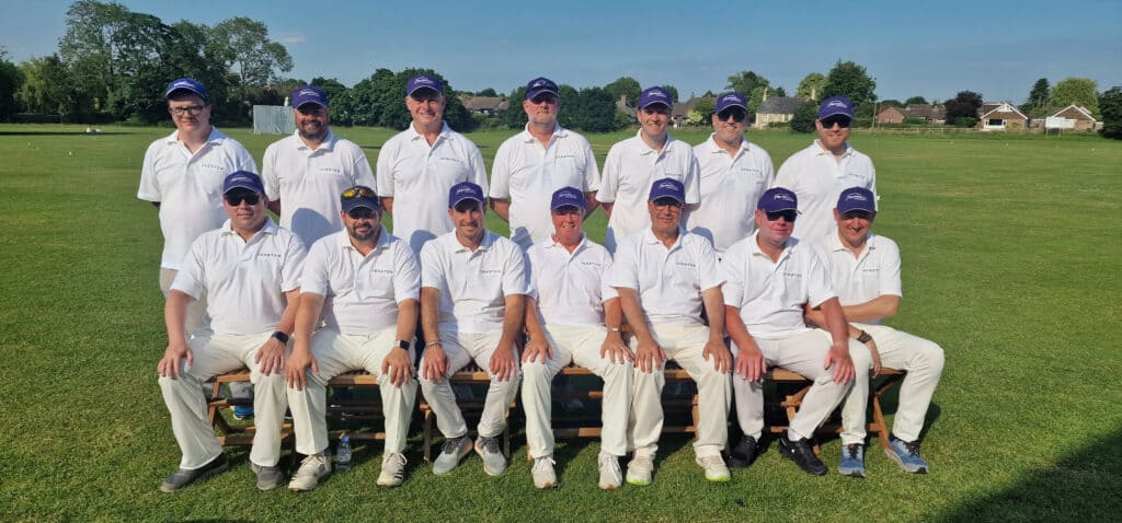Group of men in white cricket uniforms and blue caps on a cricket field.