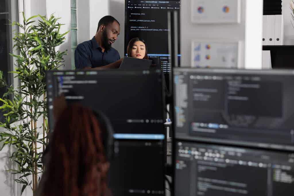Team of app developers looking at coding algorithms on laptop computer in digital software company. System programmers discussing database script and firewall server, big data interface.