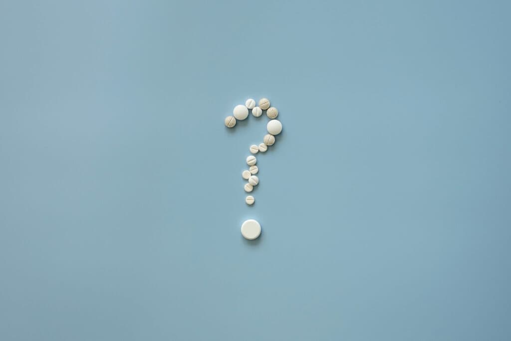 Question mark made of pills on blue background, symbolising medical or health insurance questions.