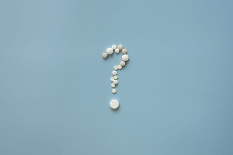 Question mark made of pills on blue background, symbolising medical or health insurance questions.