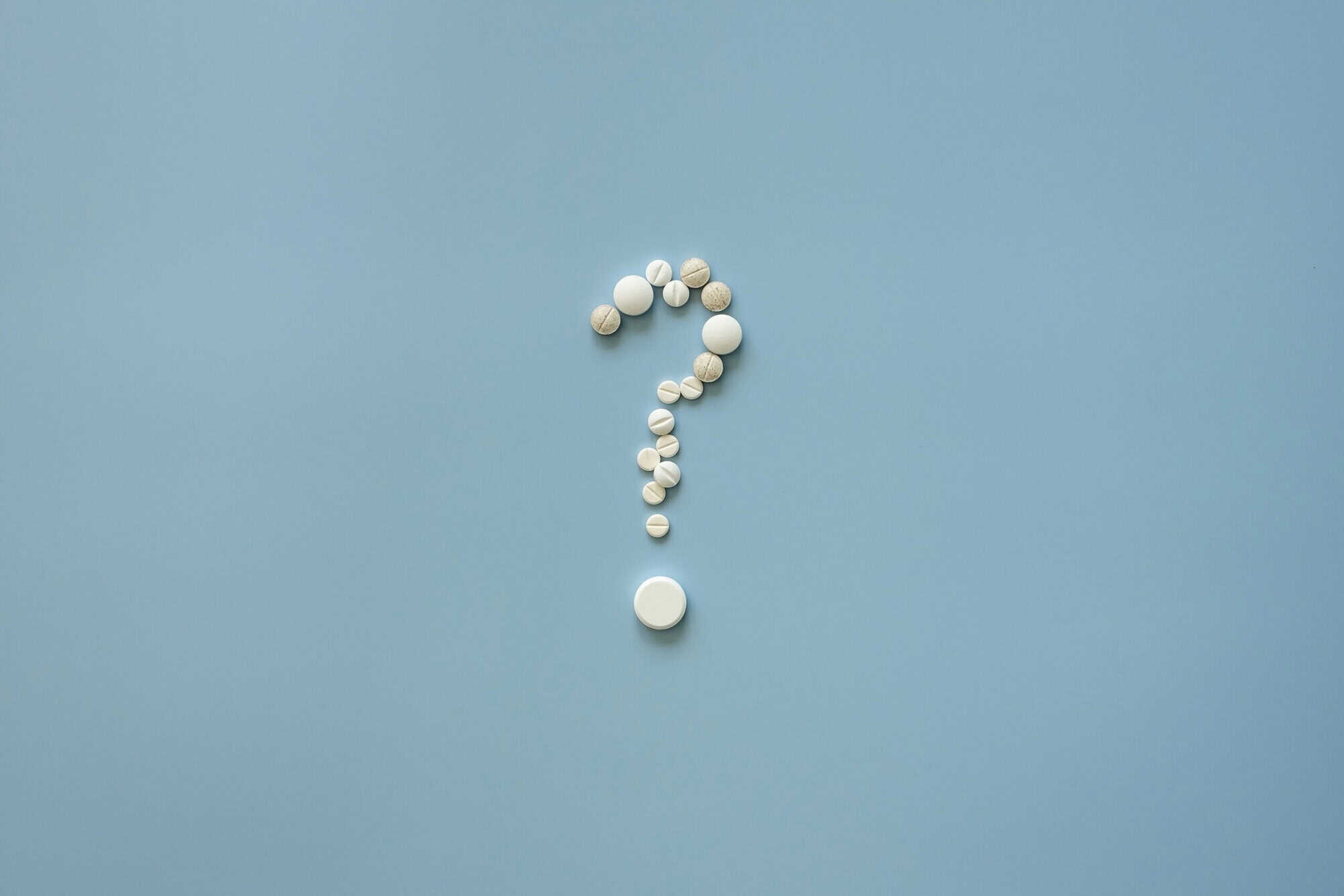 Question mark made of pills on blue background, symbolising medical or health insurance questions.