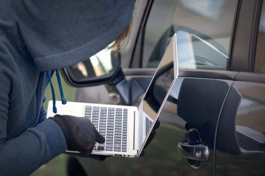 Cyber Hacker breaking into Motor Trade car's security systems with laptop.